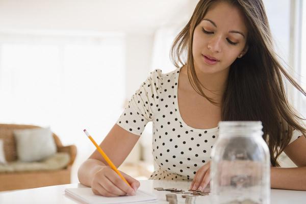 Young girl holding pencil and writing in notebook while coins are on the table 