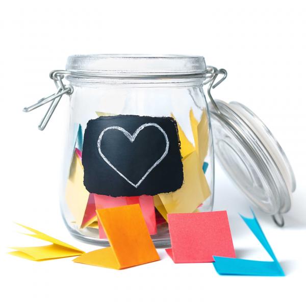 Open glass jar with folded strips of colorful paper inside