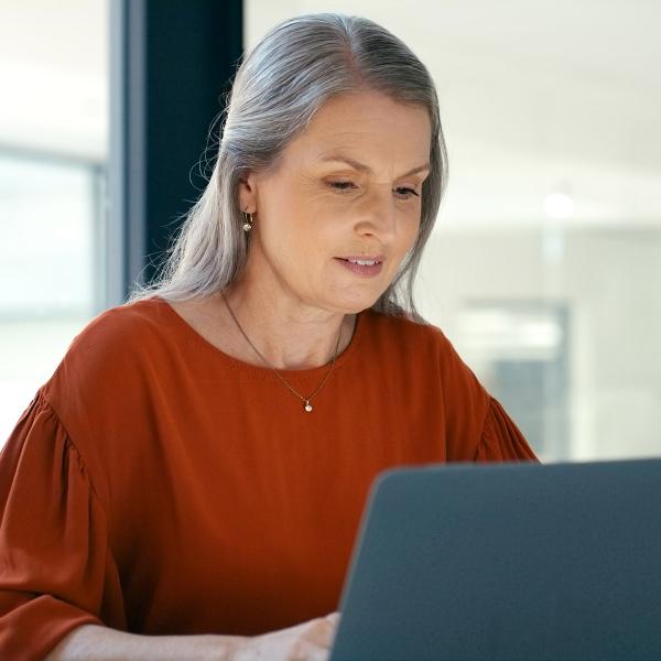 Woman with gray hair working on laptop.