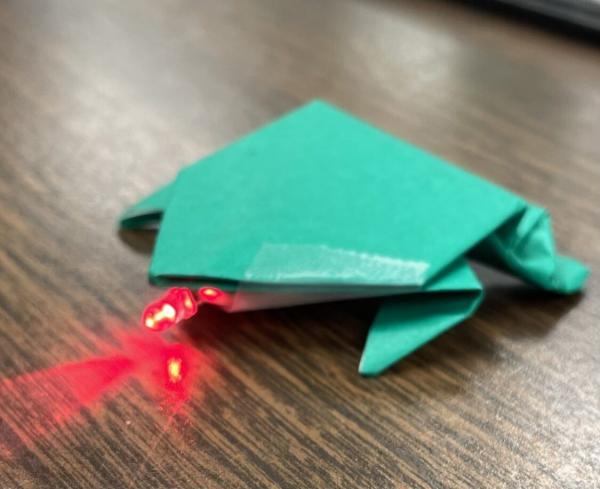 Green origami frog with light shining out of its mouth