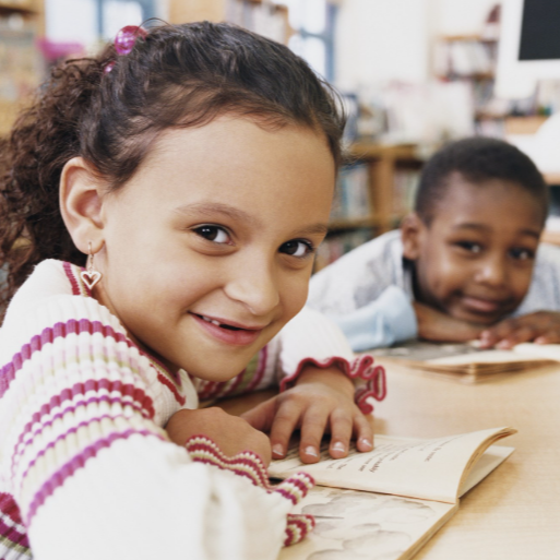 two children smiling with books at a table