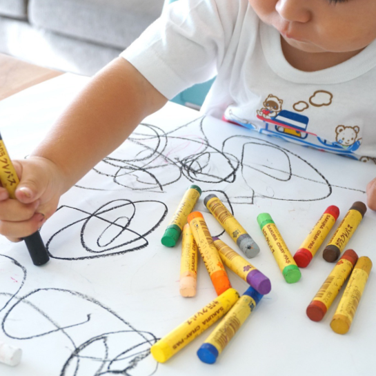 toddler scribbling on paper with crayons