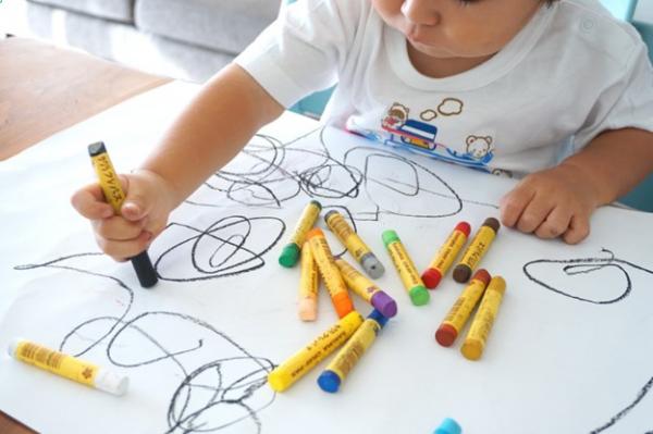 Toddler using crayons to scribble on white paper 