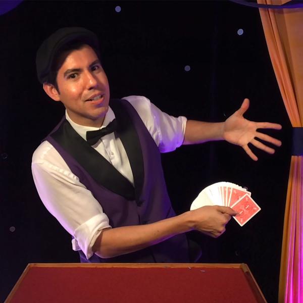 Magician in vest and bowtie brandishes playing cards with flourish