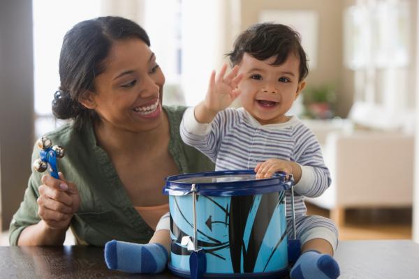 Baby tapping a drum with smiling woman lookin on