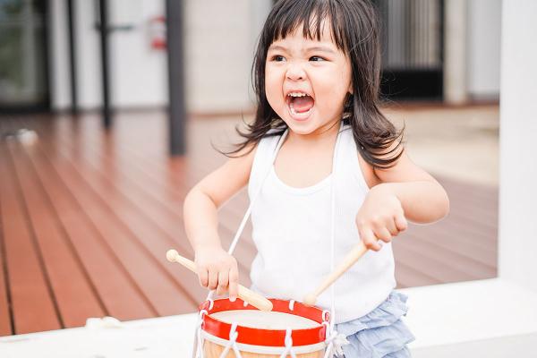 Baby playing drum with sticks. Mouth open, singing. 