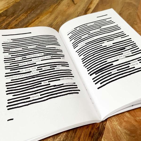 Open book laying on table with lines blacked out