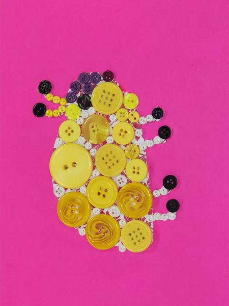 A ladybug made out of yellow and white buttons with a black face, toes, and tips of antennae on a pink background.