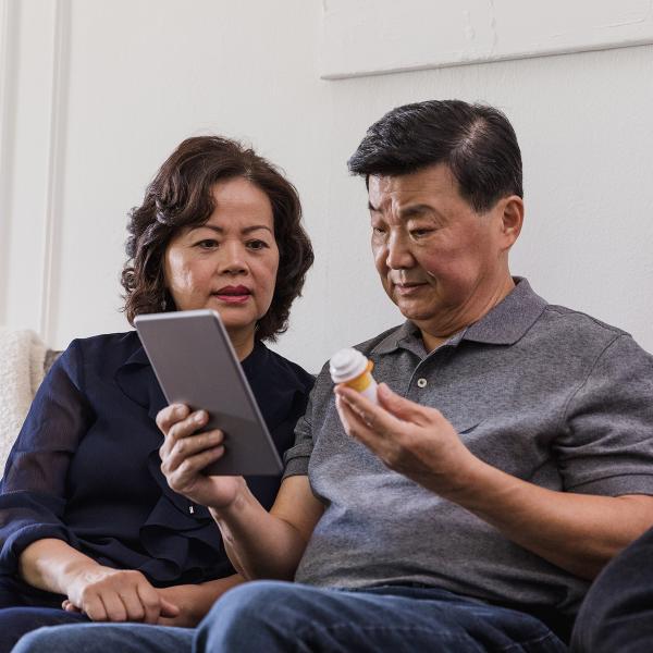 Couple looking at tablet with man holding pill bottle.