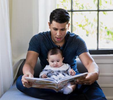 A man sits with a baby in his lap while reading a picture book