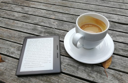 An eReader and a cup of coffee on a wooden tabletop.