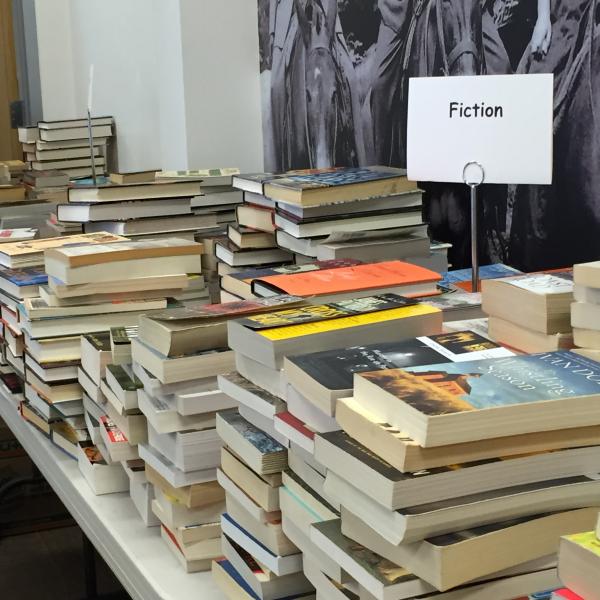 Piles of books on a table with a sign reading, "fiction."