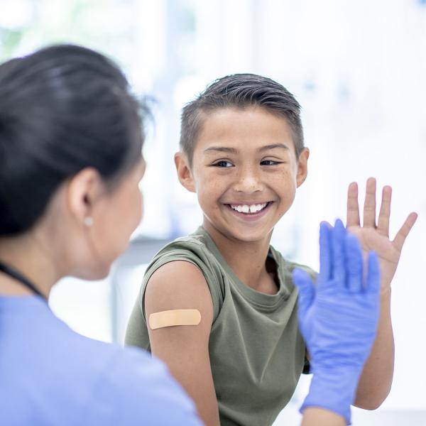 a woman in scrubs high fiving a child who just received a vaccine and has a bandaid on his shoulder.