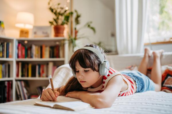 Girl with headphones writing in a notebook.