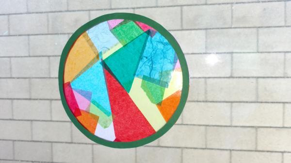 Round tissue paper suncatcher with black border and multicolored shapes inside.