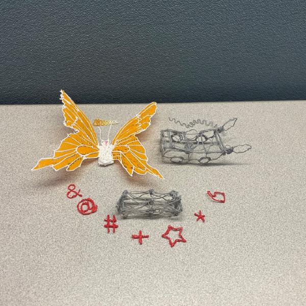 3D printed plastic objects arranged on a table including a butterfly, car the symbols: & @ # + * and star