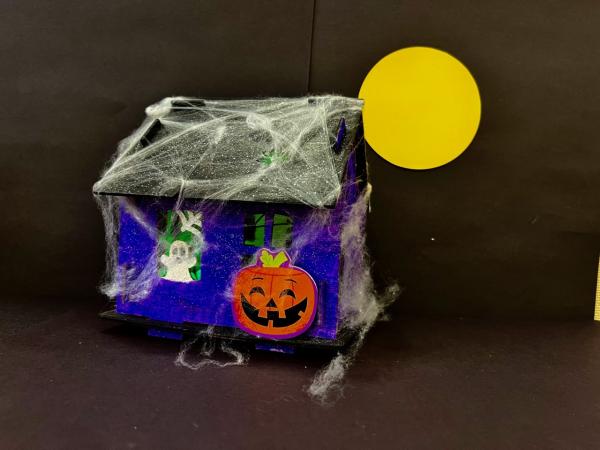 Miniature blue house covered in cobwebs with a ghost and jack-o-lantern.
