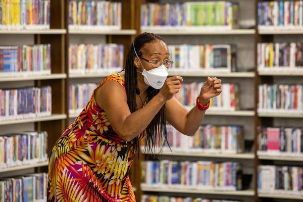 A masked African American woman leaning forward with arms in front of her as she tells a story.