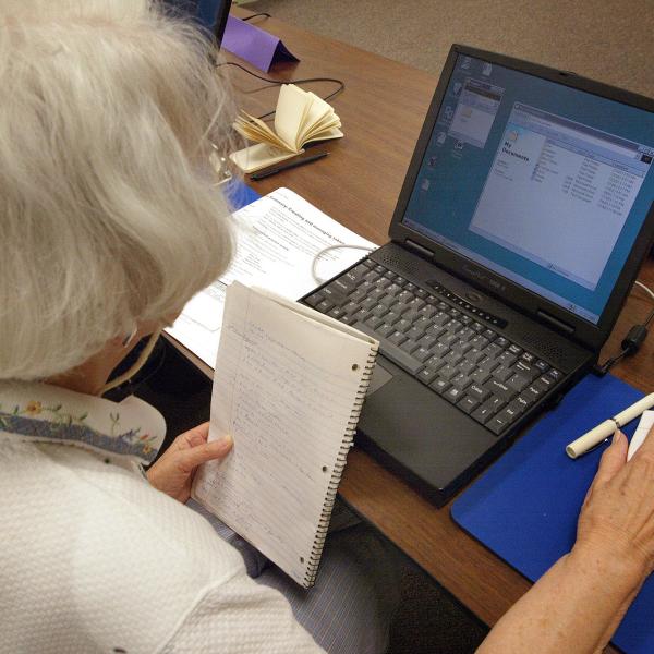 Older woman with notebook working on laptop.