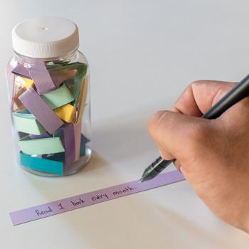 Paper strips in a jar and person writing on a strip of paper 