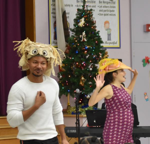 Two opera singers in hats singing in front of a Christmas tree