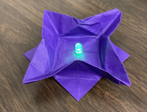 Purple origami flower with a green light in the middle.