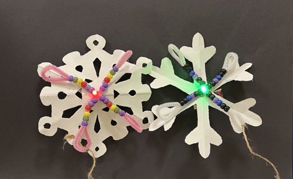 paper snowflake with folded chenille stick in cross formation with various colored bead pattern and light at the center