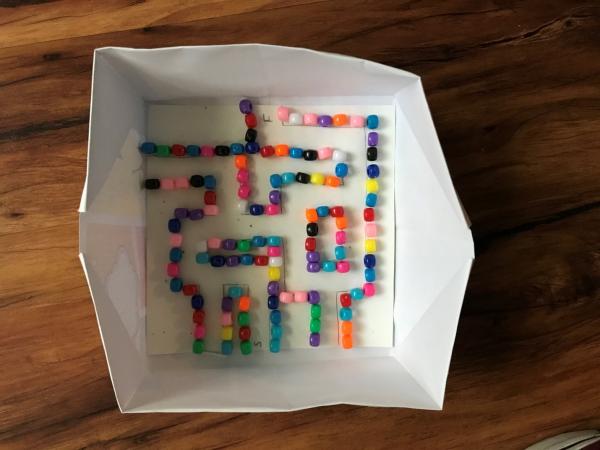 box paper in a box shape with beads positioned along the inside in various patterns to make a maze
