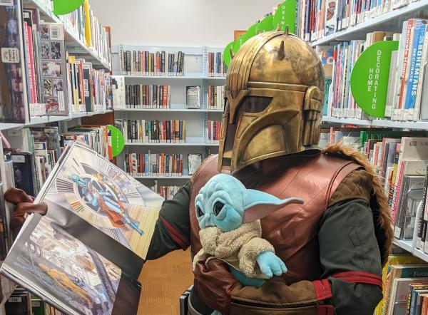 A Mandalorian reading a book with baby Yoda