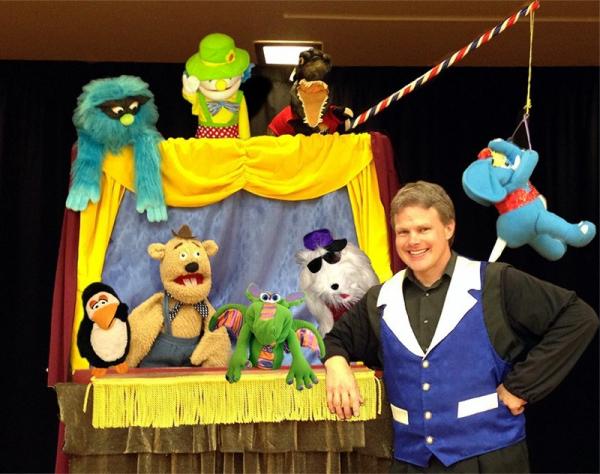 A puppet stage with yellow curtains surrounded by various puppets and a man in a blue vest.