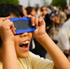 Child looking through eclipse viewer and smiling, surrounded by people in blurry background