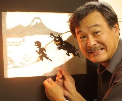 Sunny Seki holding shadow puppets in front of a shadow puppet stage.
