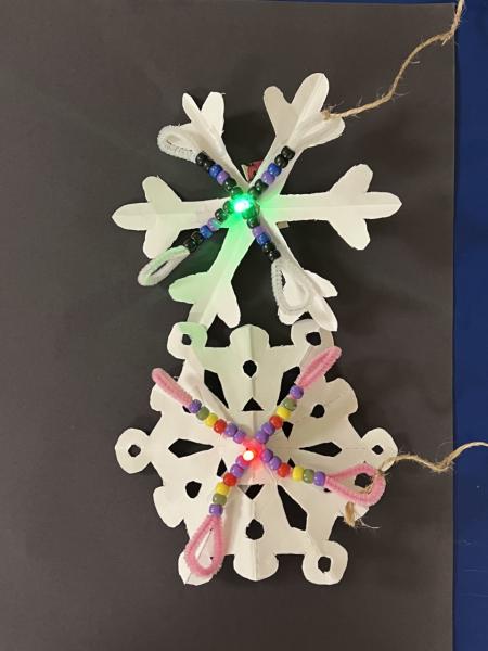 Paper snow flakes decorated with beads and pipe cleaners and glowing LED lights.