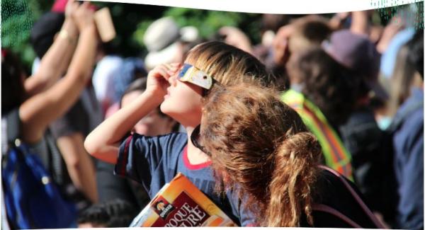 A child in a crowd uses solar eclipse glasses to safely view the solar eclipse.