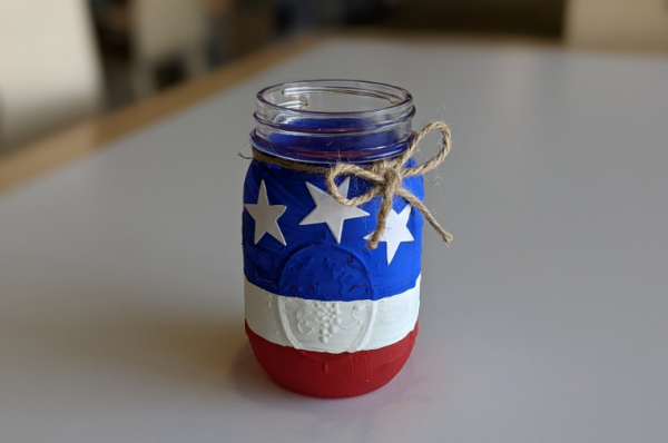 Mason jar painted red, white, and blue and embellished with white stars and twine.