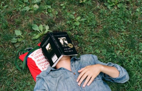 A person napping on the grass with a book over their face.