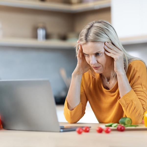 Women looking at laptop with hands on sides of head, stressed out.