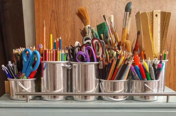 Aluminum cups filled with art materials like scissors, colored pencils, paintbrushes and rulers 