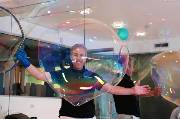 A smiling man standing behind a giant bubble.