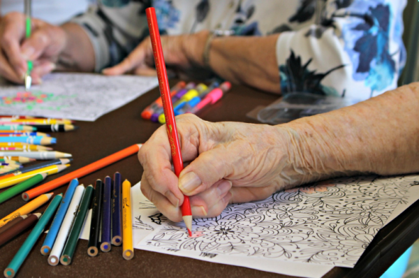 three adults around a table coloring with colored pencils