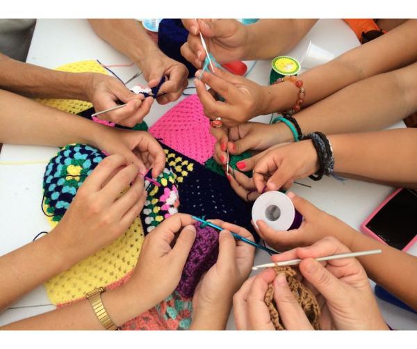 A picture of a group of hands holding crochet hooks and yarn.