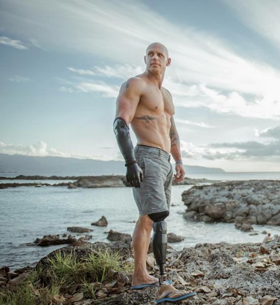 Photo of de Gelder standing shirtless on a rocky beach in front of the ocean.
