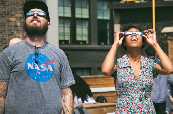 Photo of people observing an eclipse through solar eclipse glasses.