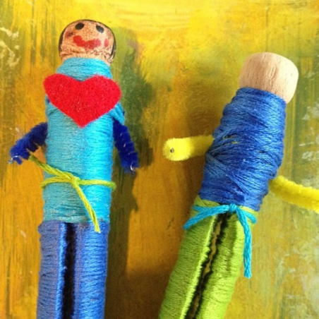 two wooden doll pegs wrapped in colorful yarn
