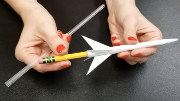 Two hands holding a pencil and a rocket made out of paper 