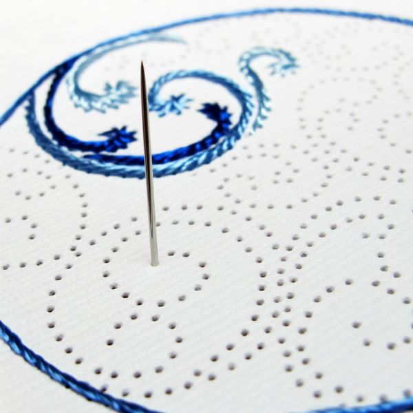 white paper with holes in a wave design with a needle and blue thread