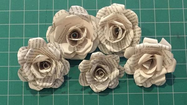 Paper roses made from book pages on a green gridded cutting mat
