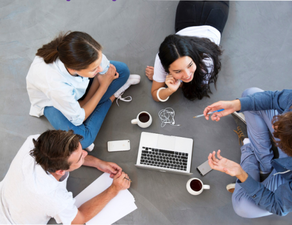 Teens sitting on the floor in a circle, collaborating around a laptop