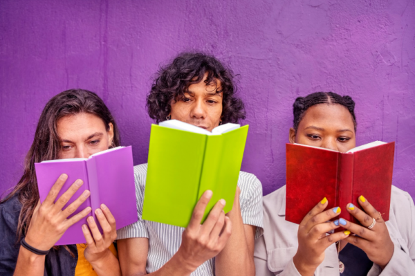 Three teens holding an open book in front of them 